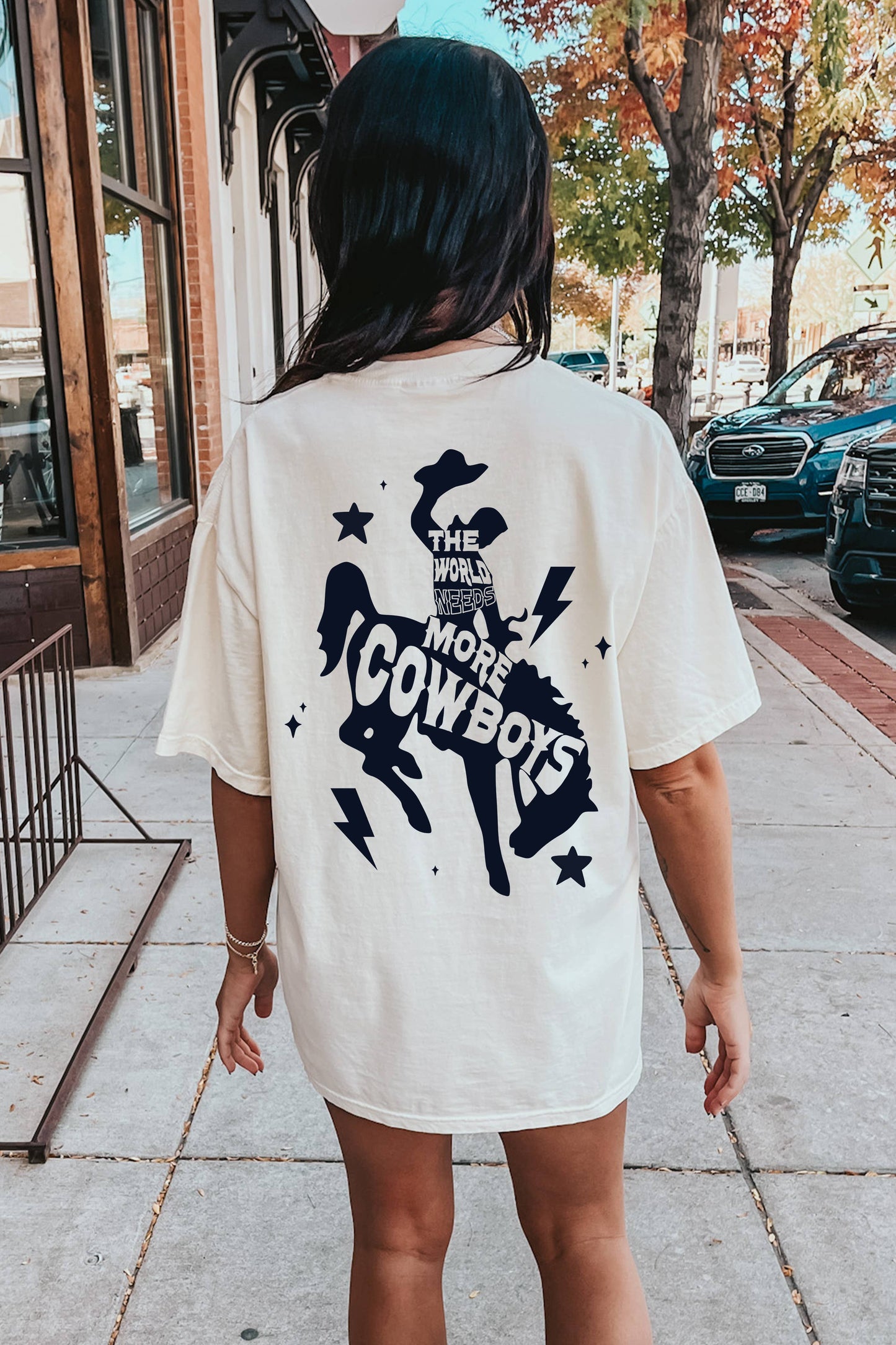 Person wearing a white t-shirt with a 'The World Needs More Cowboys' graphic.