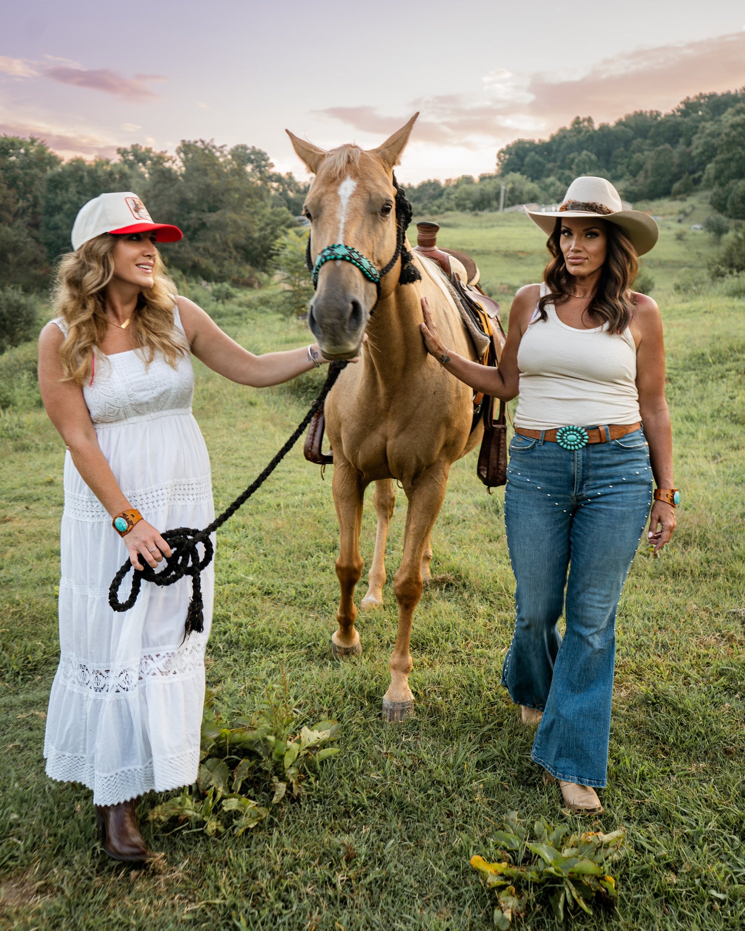 Two women walking a horse in a grassy field with a scenic background