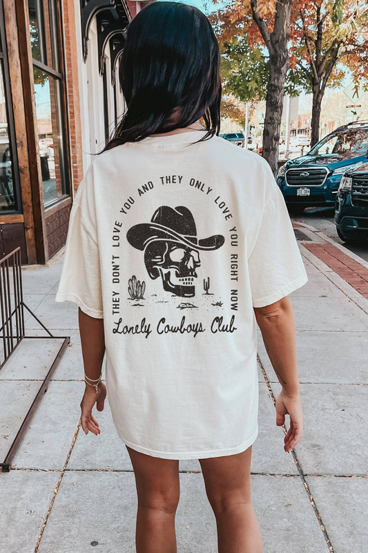Person wearing a white t-shirt with a graphic design and text that says 'Lonely Cowboys Club' with a skull graphic on the back.